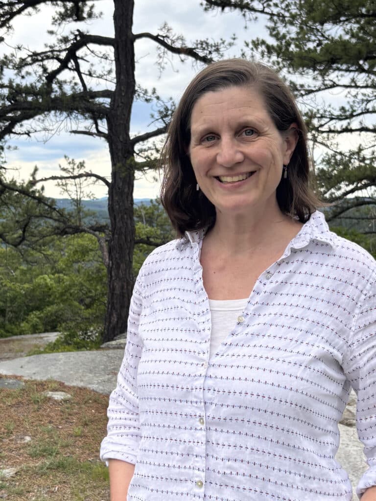 Portrait of a woman on a rocky hilltop with wooded hills behind